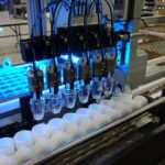 Pneumatic pick-and-place with custom grippers moves bottles from a box and into individual fixtures.